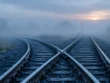 Δύο σιδηροδρομικές γραμμές που διασταυρώνονται μέσα στην ομίχλη, με κόκκινο σηματοδότη στο βάθος και την ανατολή πίσω του