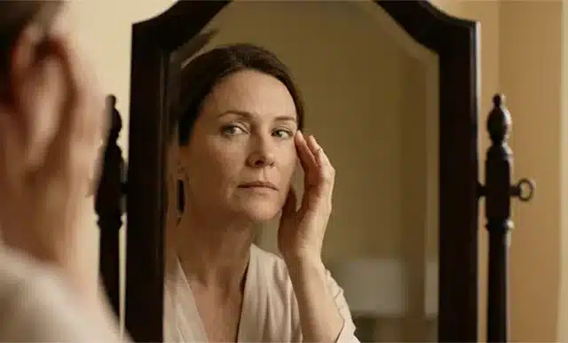 Γυναίκα κοιτάζει το πρόσωπό της στον καθρέφτη σκεπτόμενη το botox και την αυτοεικόνα