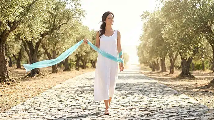 Μια γυναίκα σε ένα ηλιόλουστο δρόμο, με μια ημιδιαφανή κορδέλα να τυλίγεται ελαφρά γύρω από τον καρπό της.